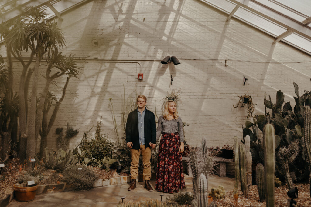 Maryland engagement session location in a greenhouse with a couple holding hands in a room filled with cactus
