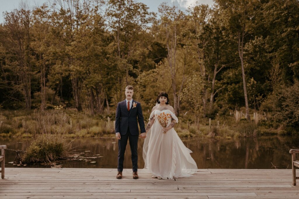 Affordable Maryland outdoor wedding venues in an open nature field. Bride and groom stand holding hands by the water