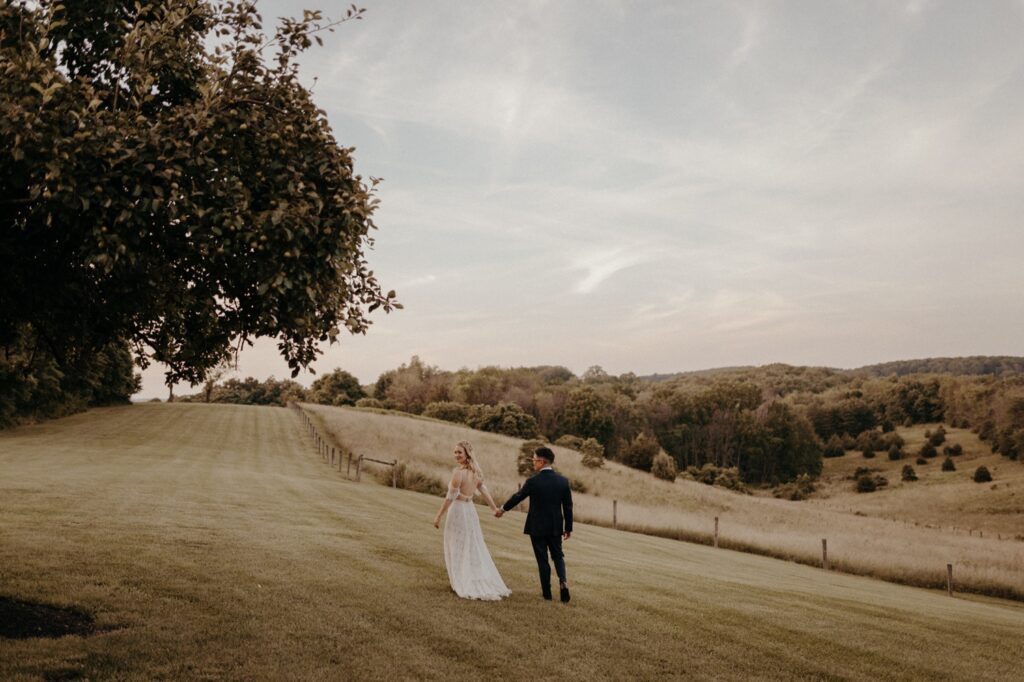 Bride and groom walking through open field and rolling hills in the mountains of a wedding venue