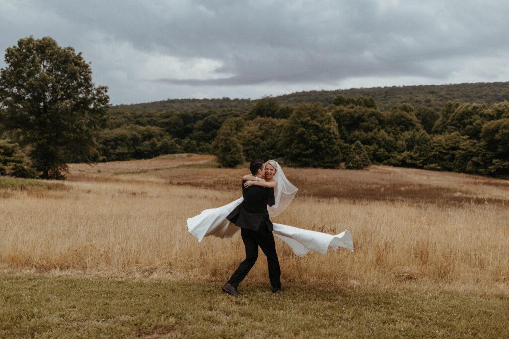 Bride and groom laughing in a grassy field with mountain backdrop at Maryland outdoor wedding venues