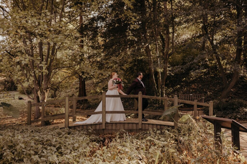 Garden wedding venue in maryland with nature, a greenhouse, and a bride and groom walking over a bridge in the woods